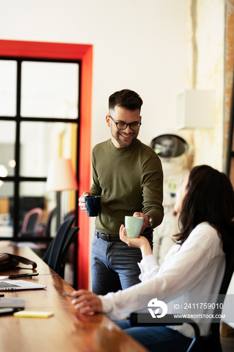 Colleagues drinking coffee in office. Businesswoman and businessman discussing work in office