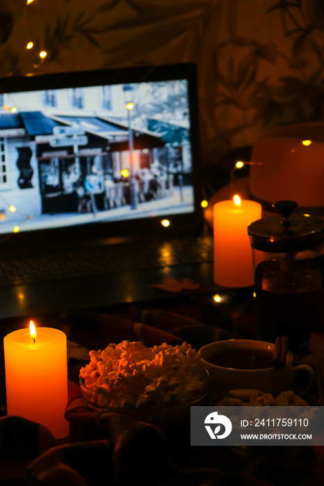 Movie on laptop at night in bedroom lit with candles. Pop corn. Autumn atmosphere at home