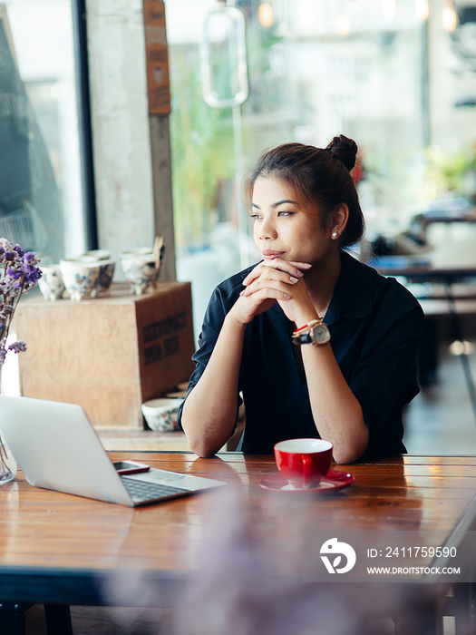 Asian woman working in cafe and looking out window..