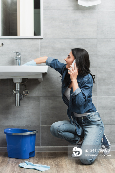 Smiling woman talking on phone while repairing faucet