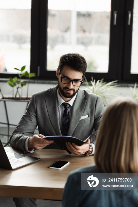 Businessman in suit holding resume near blurred woman during job interview in office.