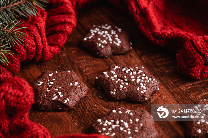 Star shaped chocolate shortbread cookies on a wooden background near a knitted sweater and spruce branches. Christmas mood.