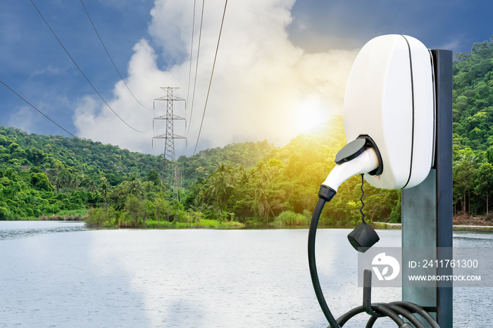 Ev station plug and power cable supply for electric vehicle charging or hybrid car on natural blue sky sunshine and high voltage electric pole at river and green mountain background