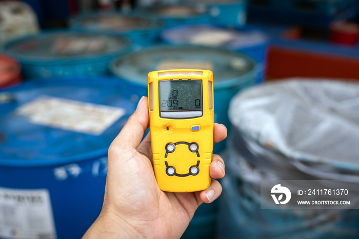 Using a portable gas detector to monitor the air or toxic gas composition around the chemical storage area (with blurred background of chemical barrel). Industrial action and object photo.