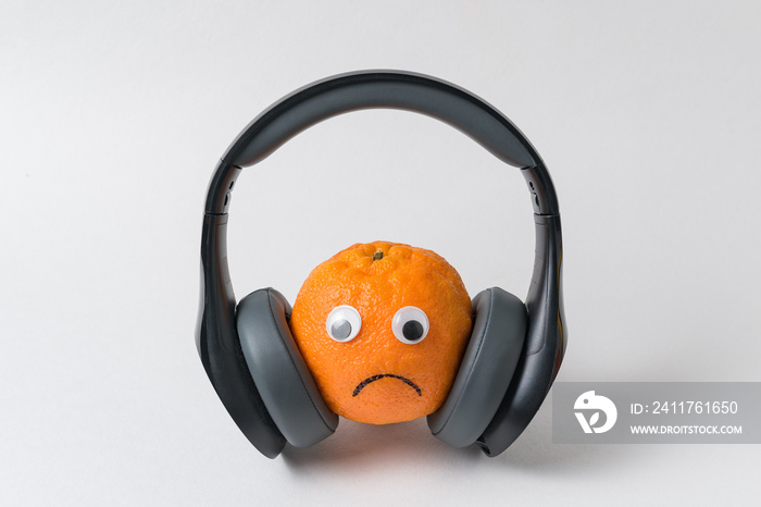 Orange with sad face in big headphones. Too much noise concept