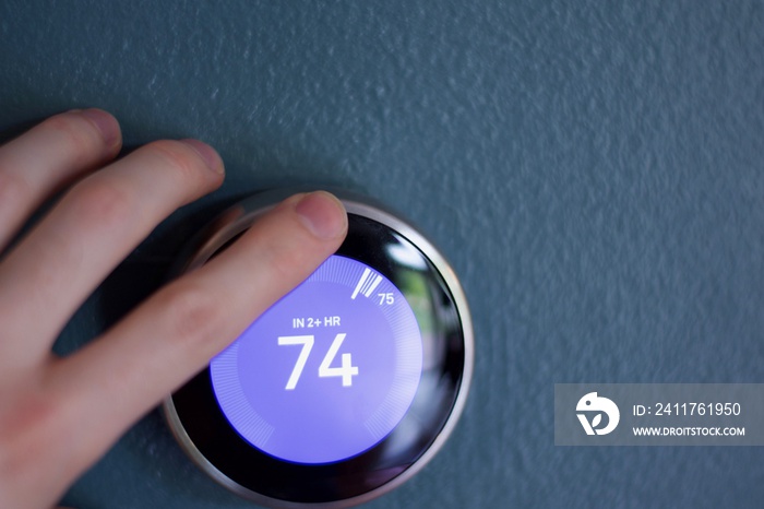 Male Hand changes temperature of smart home thermostat on blue wall in Fahrenheit  .