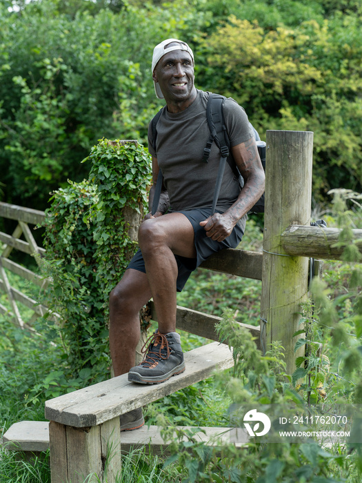 Smiling mature man sitting on fence on hike