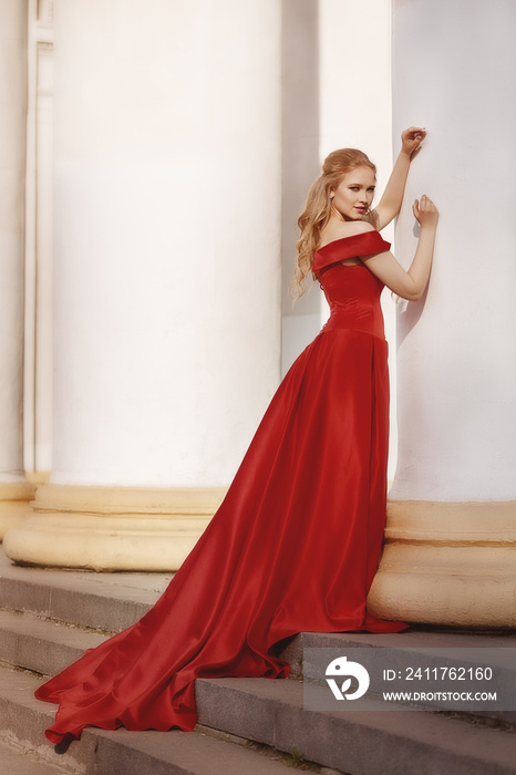 Beautiful blonde girl in a red long dress on a background of architecture, columns