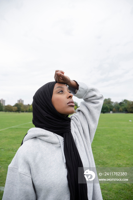 Portrait of woman in hijab standing in soccer field, touching forehead