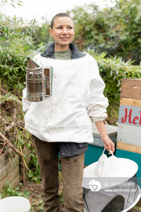 Portrait of smiling female beekeeper holding smoker in urban garden