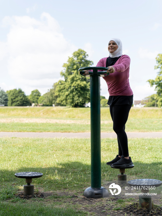 UK,Sutton,Smiling woman in headscarf exercising at park gym