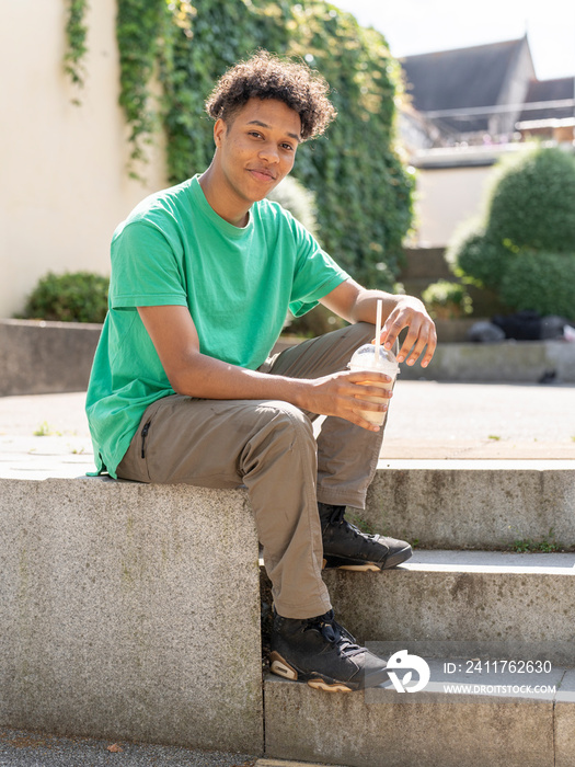 Portrait of young man sitting on stone wall with smoothie