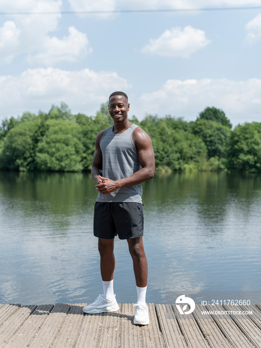 Portrait of smiling muscular man in sports clothing standing by lake