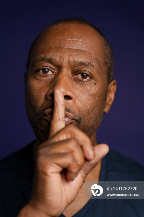 Portrait of man with finger on lips against purple background