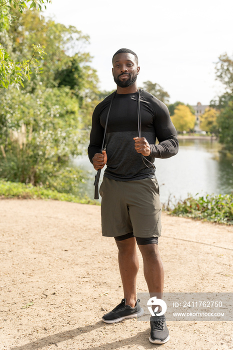 Portrait of smiling athletic man with jump rope in park