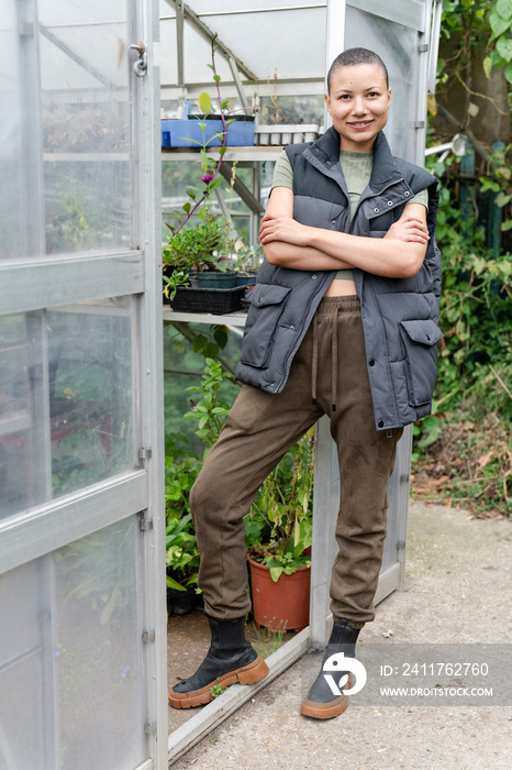 Portrait of smiling woman standing in front of greenhouse