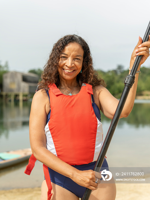 Portrait of smiling woman standing with oar by lake