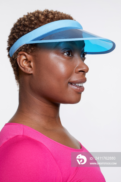 Profile of smiling woman wearing blue sun visor and pink shirt