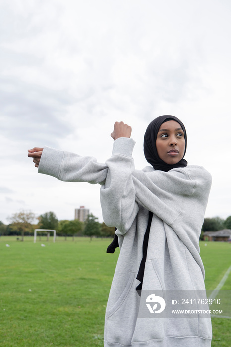 Portrait of woman in hijab stretching arm in soccer field