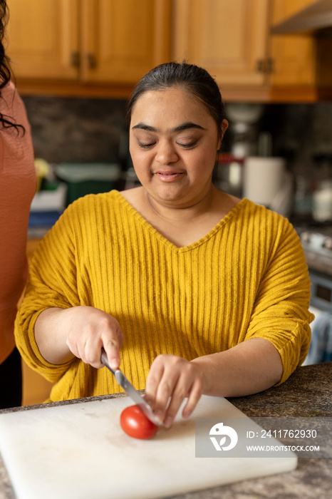 Young woman with down syndrome cutting tomato in kitchen