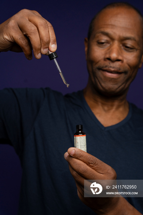 Portrait of man taking medicine with pipette against purple background