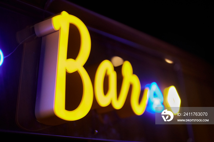 Neon inscription BAR on the wall. Neon inscription BAR in yellow. Yellow neon inscription BAR on a dark background