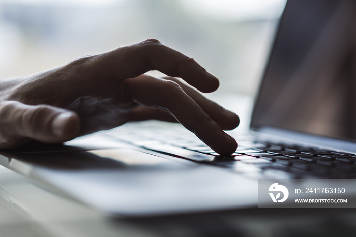 Businessman typing on laptop keyboard in sunny office, business and technology concept. Close up