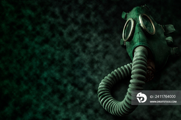 Armageddon, biological warfare and post apocalyptic survivor conceptual idea with green rubber gas mask surrounded by toxic smoke and radioactive dust on dark grungy background with copy space