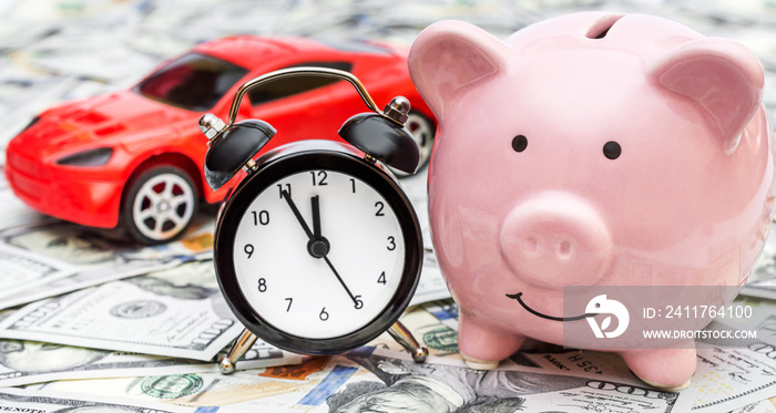 Piggy bank with alarm clock and car toy on background of money. Time to savings for car.