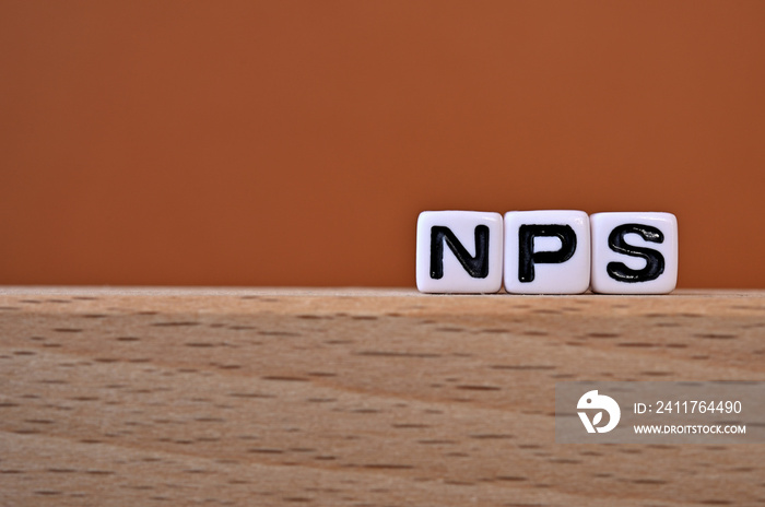 Word cubes lined up with the letters NPS written on it. It is an abbreviation for Net Promoter Score. Copy space available.