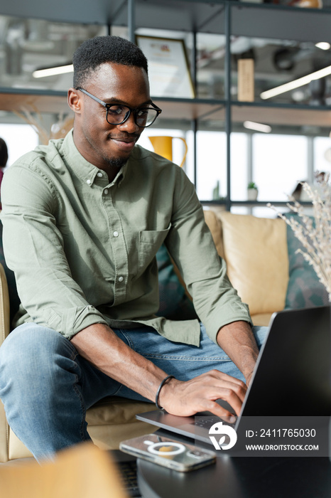 Young man with laptop sitting in office lounge