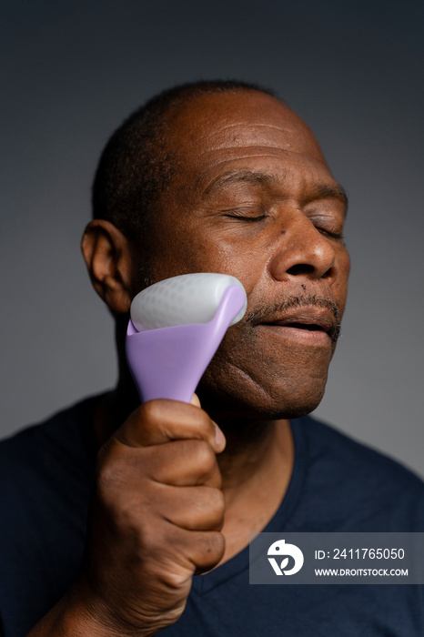 Portrait of man doing face massage with roller