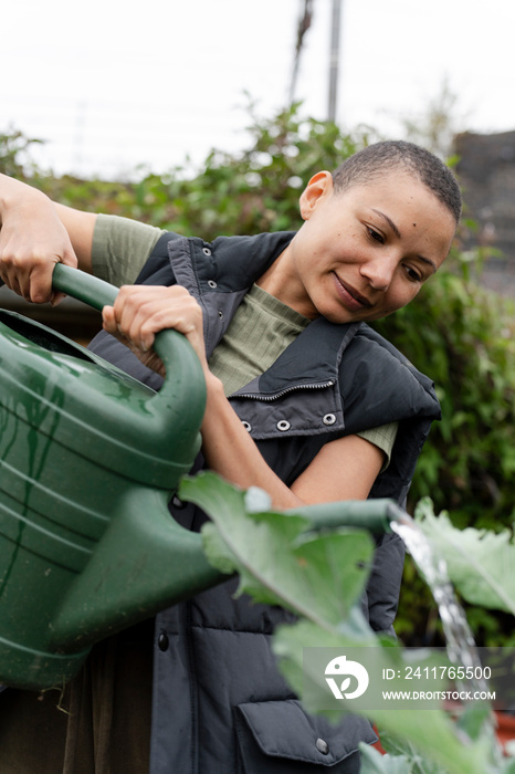 Smiling woman watering homegrown vegetables in urban garden