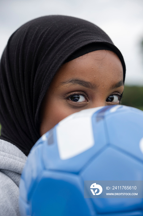 Close-up of woman in hijab with soccer ball in front of face