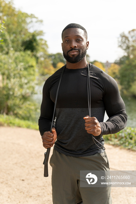 Portrait of smiling athletic man with jump rope in park