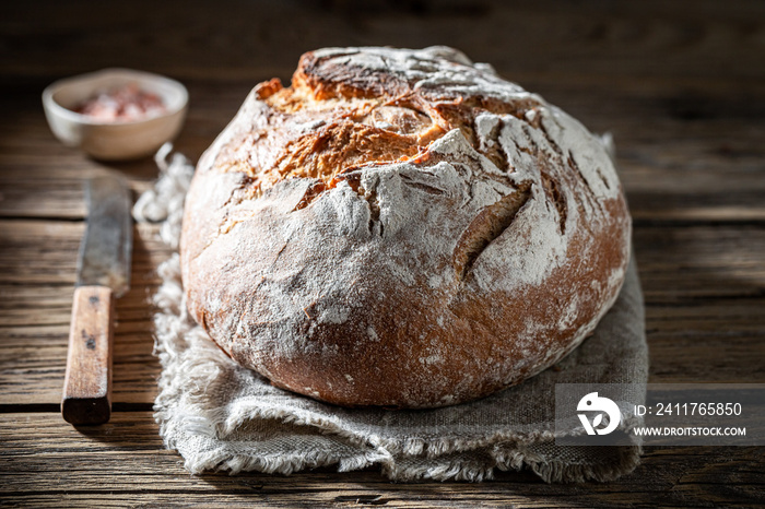 Fresh loaf of bread with salt on wooden table