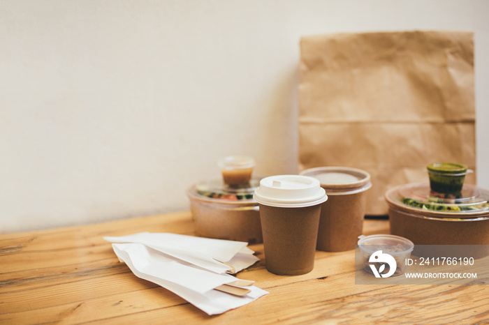 Takeaway food in containers and disposable bowls on wooden table on white background. Food delivery and takeout. Place for text.