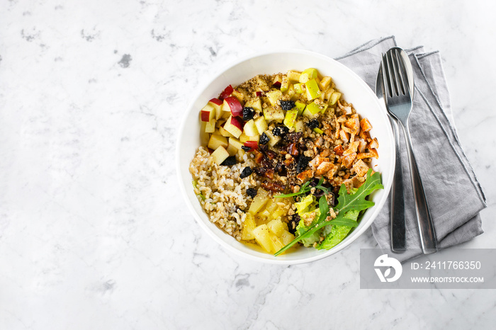 Salad lunch bowl with mix salad, chicken breast, apple, pineapple, raising, dates, brown rice and walnut. Keto salad in bowl on marble background. Top view, copy space. Concept of healthy food