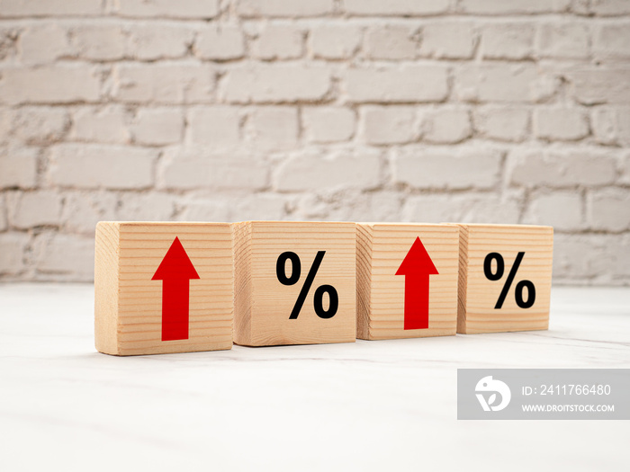 Wooden cubes with red arrows up and percent symbols on a marble floor with white brick background