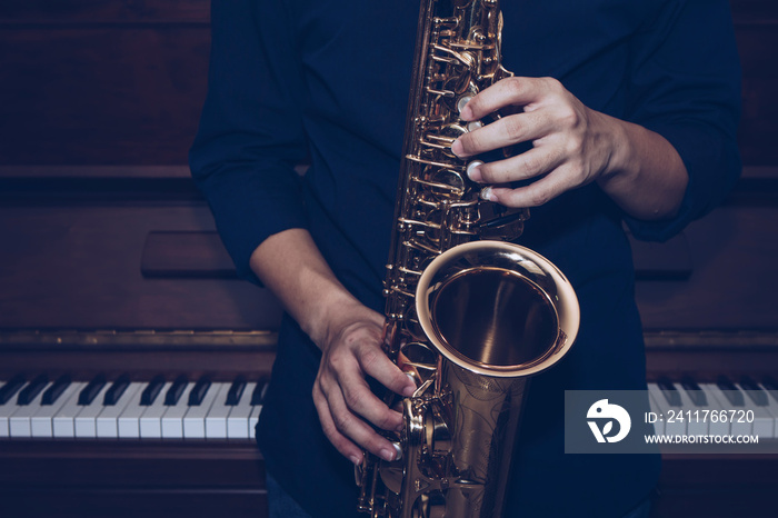 Close up of a young musician  man hands hold and playing  saxophone on black background with copy space. Can be used for music poster background