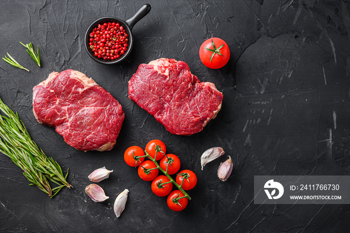 Raw rump steaks from organic beef meat cuts with rosemary, garlic and spices over black textured  background, top view space for text.