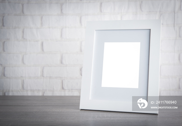 Photo frame on wood table over white brick wallpaper background