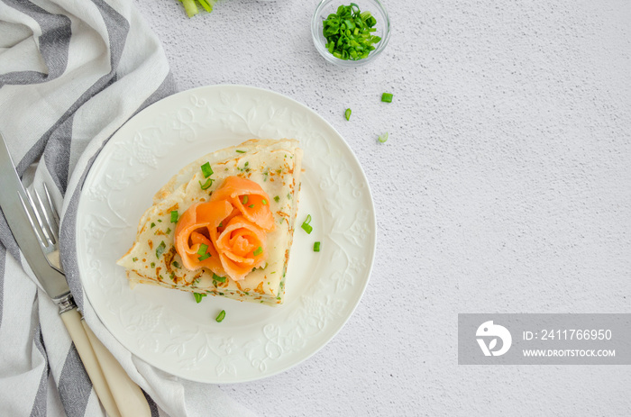 Traditional Russian thin pancakes or crepes with cheese, herbs and smoked salmon on a white plate on a light background. Holiday maslenitsa. Horizontal, top view, copy space