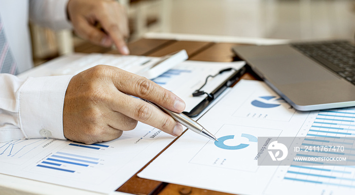 A close-up view of a businessman holding a pen pointing at a bar chart on a corporate finance document, he is meeting with senior management, with the theme of the meeting being Company Finance.