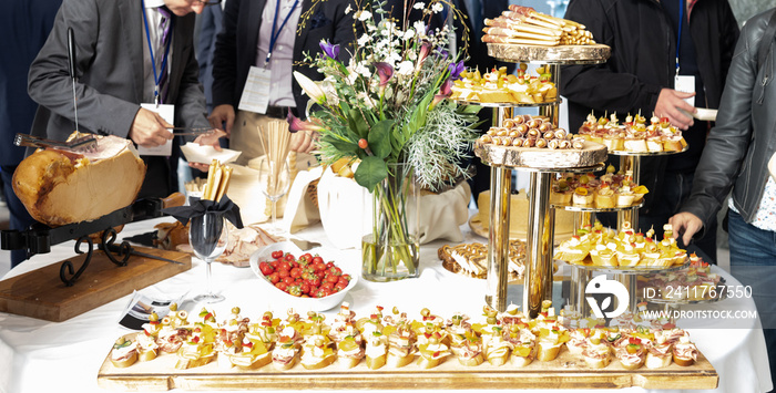 Businesspeople at banquet lunch break at business conference meeting. Assortment of canapes, small pieces of bread or pastry with a savory topping, and finger food on table.