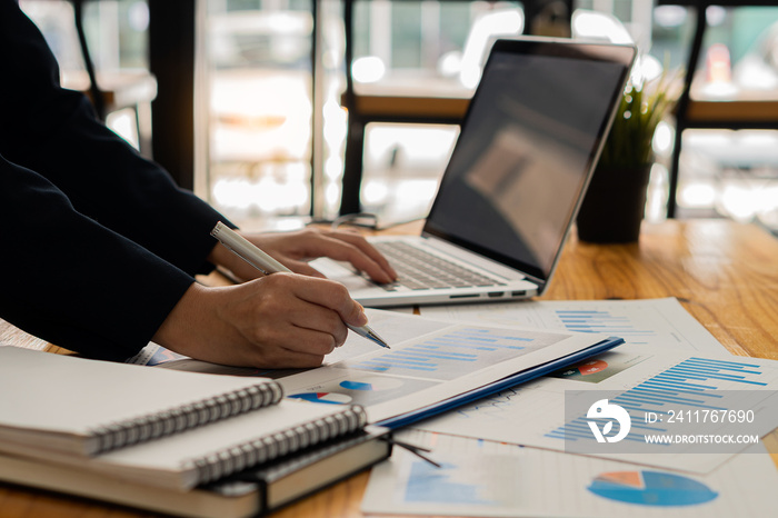 Close up of asian businesswoman hands holding pen and pointing to financial documents and investment plans for business and stocks and graph charts for investment analysis in his office