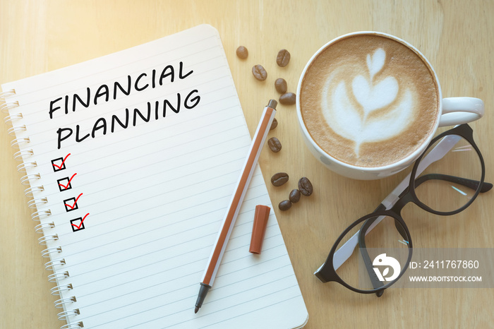 Financial Planning message and check list marks on notebook, glasses, pencil and coffee cup on wooden table with sunlight in the morning. Business concept.