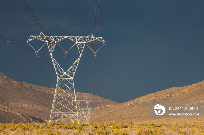 High voltage power lines running up a gorge with a storm brewing in the distance