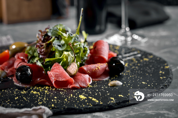 Beef carpaccio with arugula on a black plate, traditional Italian cuisine. Dark key, copy space,