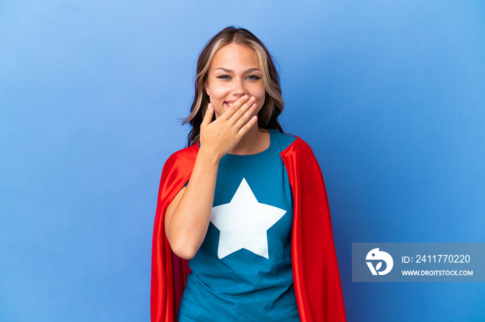 Super Hero Teenager girl isolated on blue background happy and smiling covering mouth with hand